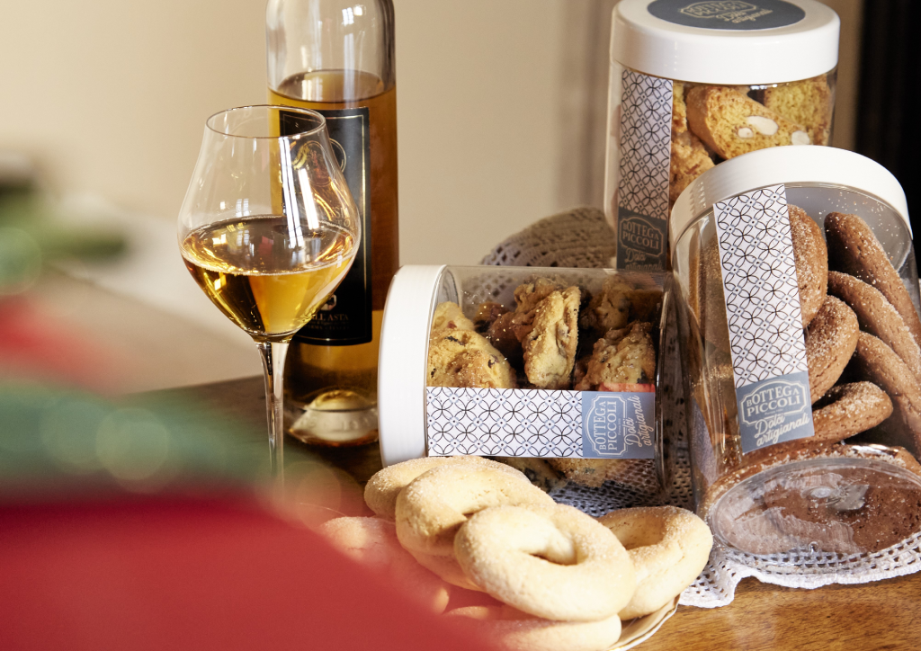 Biscotti artigianali Bottega Piccoli con vasetti e calice di vino passito su un tavolo di legno