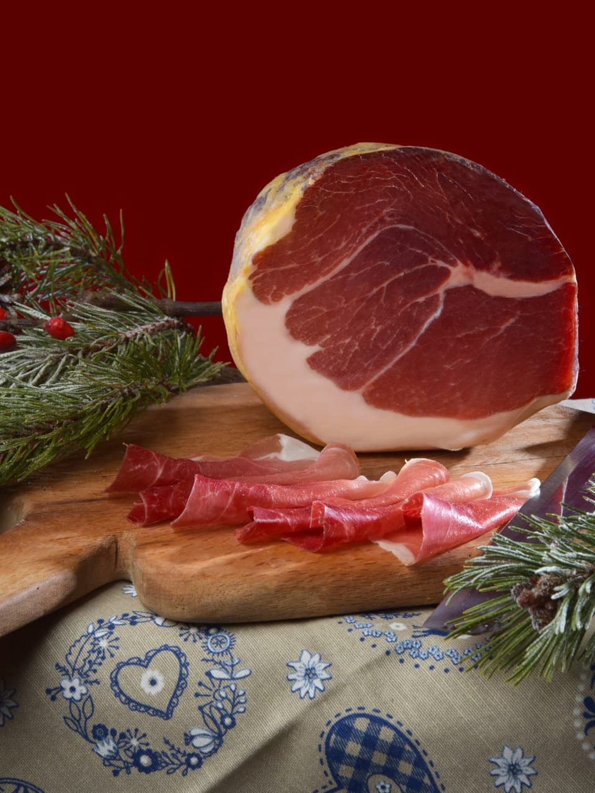 Culatello affettato su tagliere con rami di pino e pigne innevate